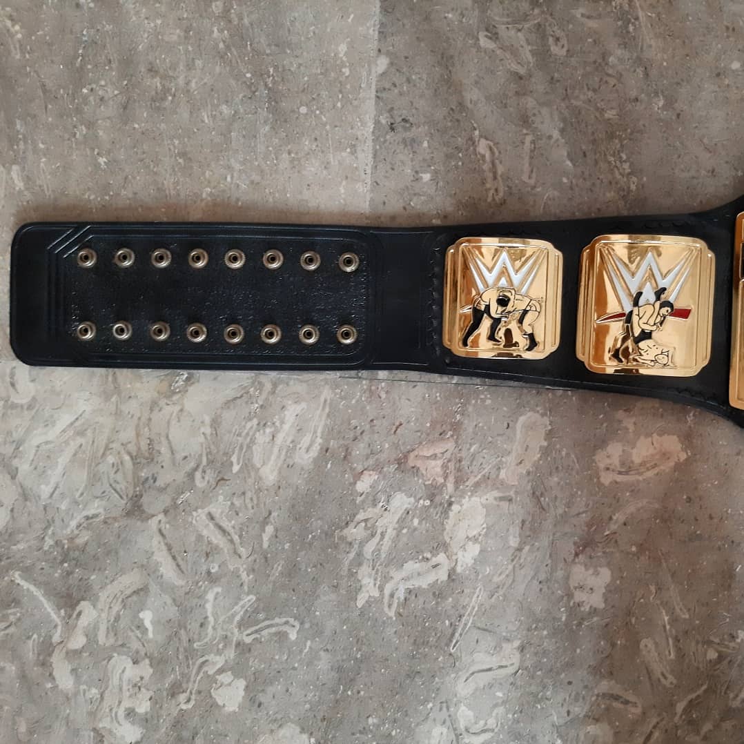 Black championship belt with gold logos on a gray surface